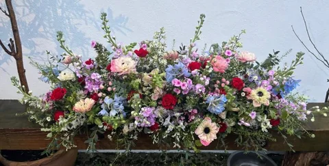 A coffin spray of reds, blues and pinks with anemones and delphiniums, like a summer garden